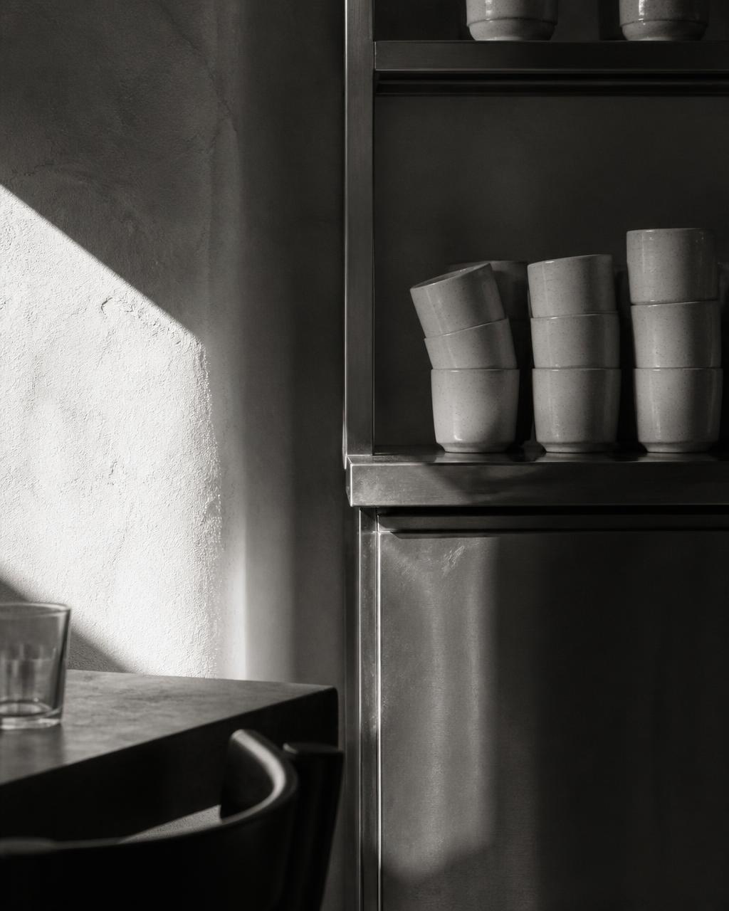 Stacked ceramic cups on a steel shelf in hard daylight