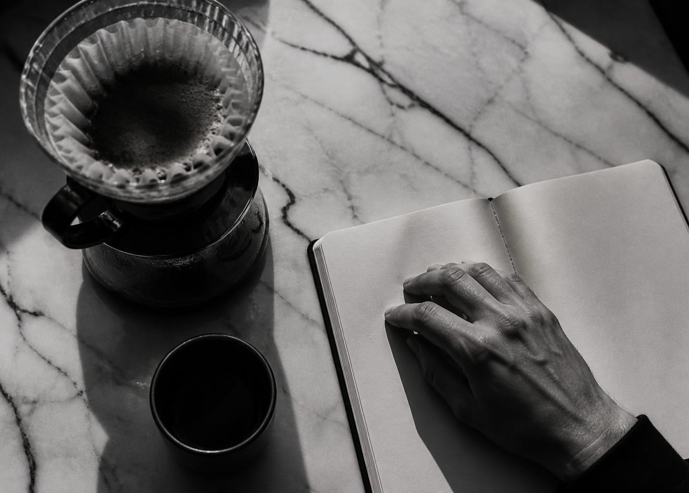 Overhead view of a filter brewer and notebook on a marble table