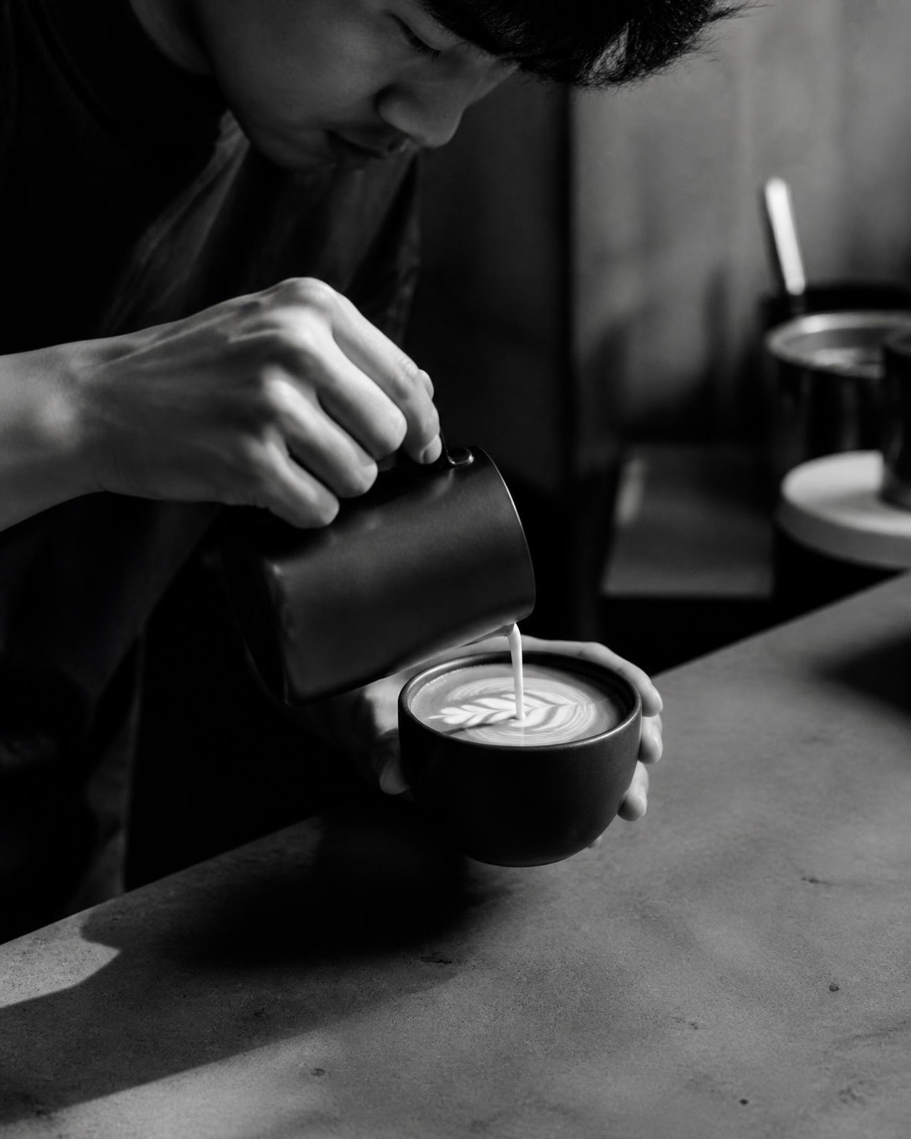 Barista pouring milk into a matte ceramic cup on a concrete counter
