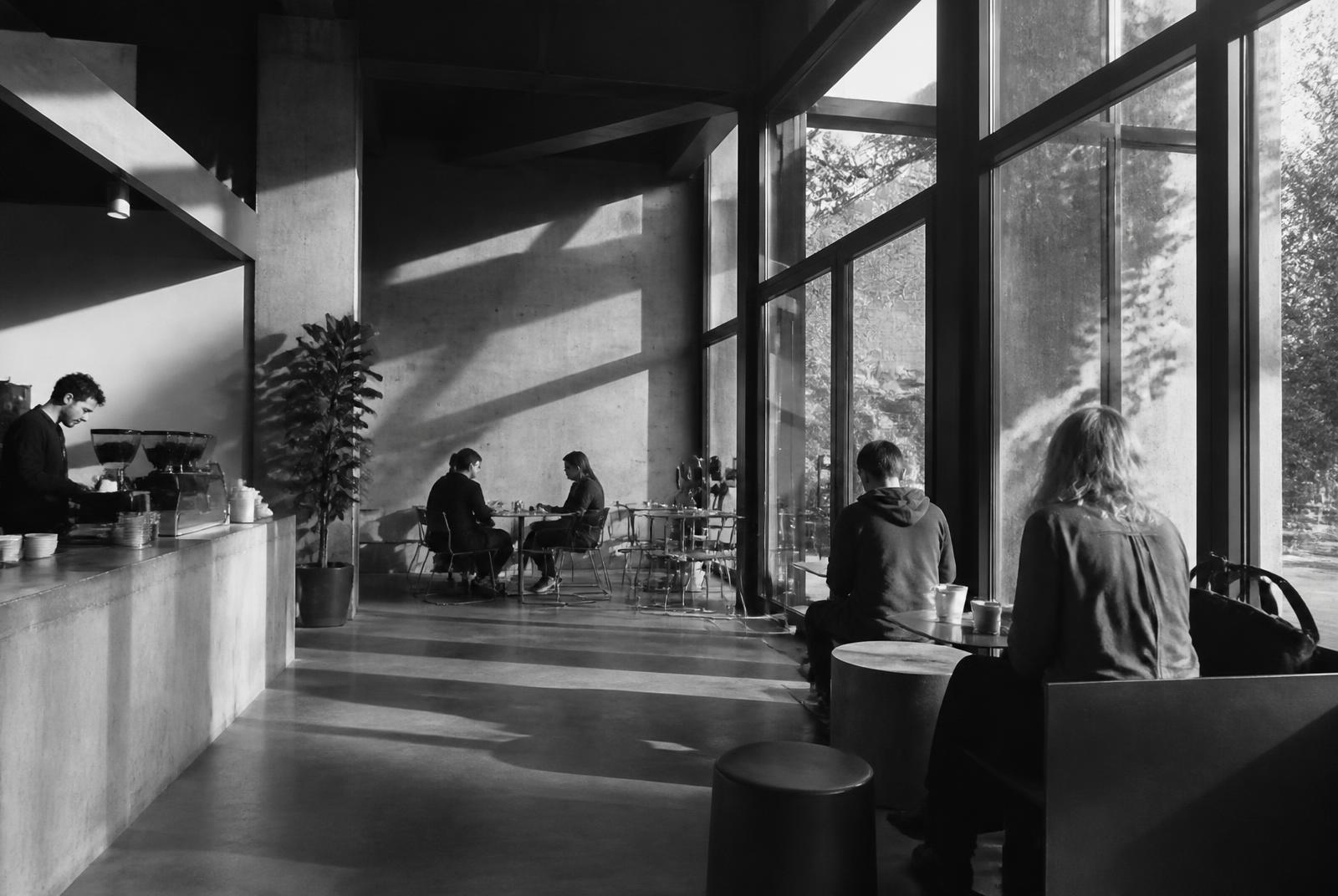 Minimal concrete coffee shop interior with large windows and people at tables